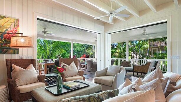 A spacious living area with a large window, comfortable seating, and a ceiling fan. - Hale Milo: Charming Garden Cottage in Sunny Poipu! (Koloa)