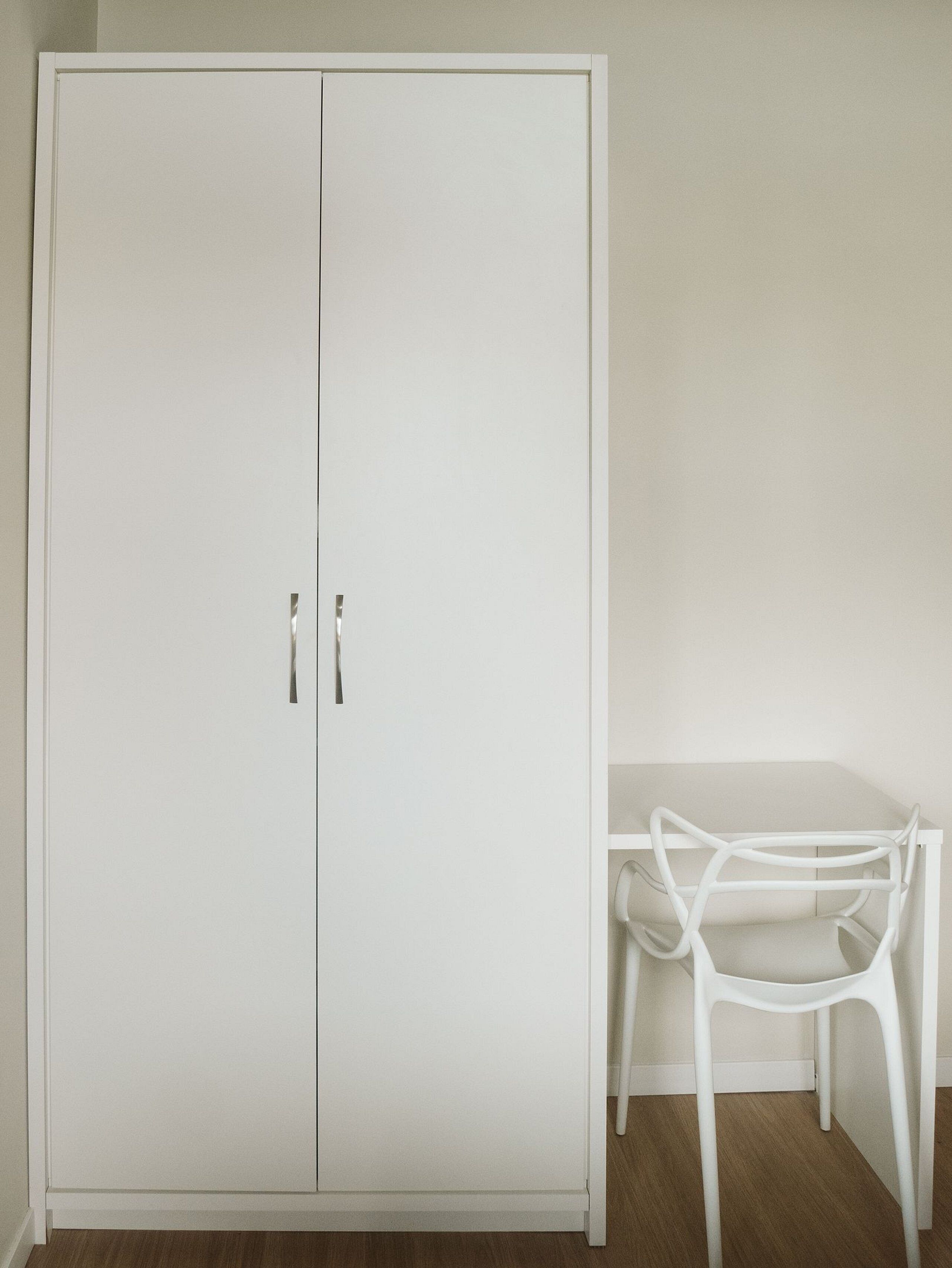 A white wardrobe with two doors and a chair with a curved backrest.