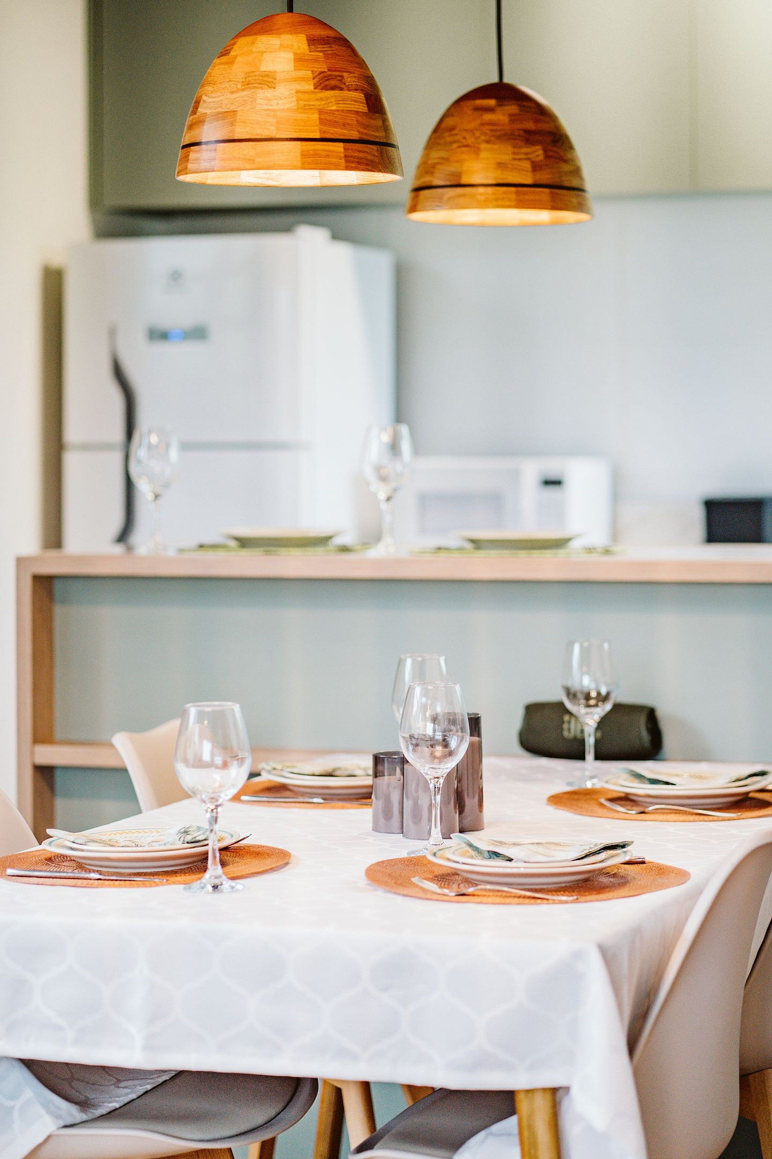 Un coin repas avec une table dressée pour quatre personnes, comprenant des verres à vin et des assiettes, sous deux lampes suspendues en bois.