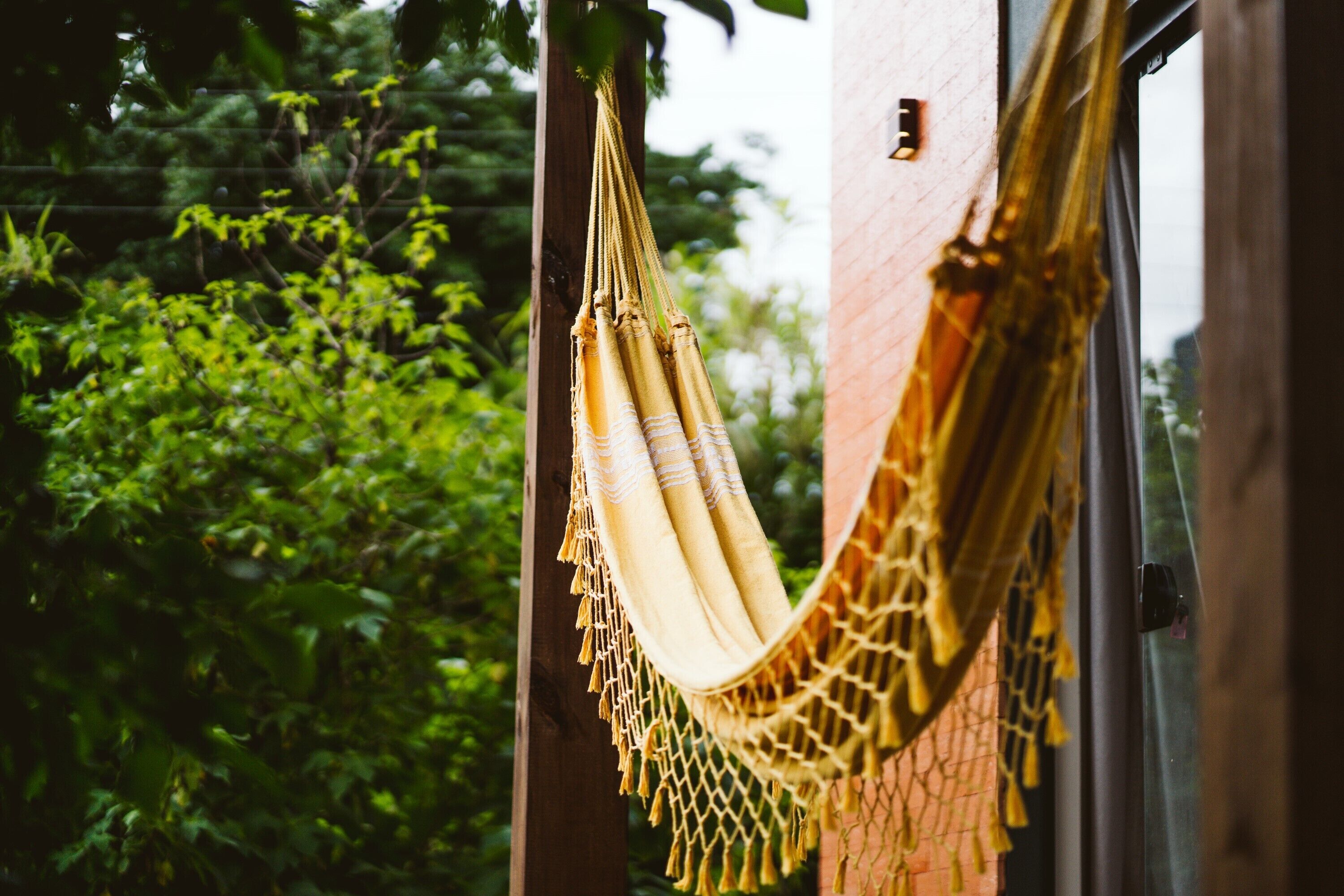 A hammock hanging between two wooden posts, with a window and greenery in the background.