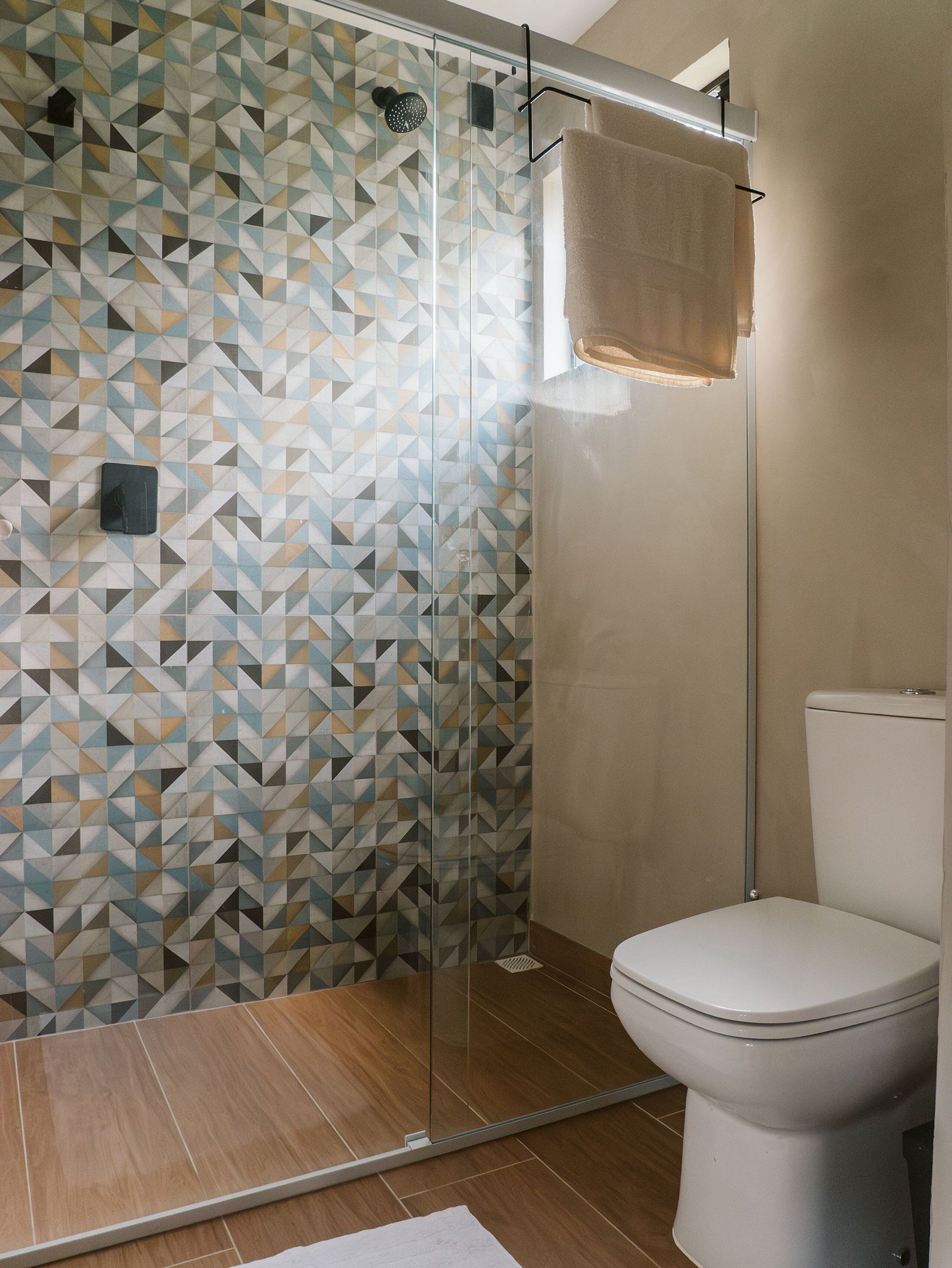 A modern bathroom with a geometric patterned shower wall, a glass-enclosed shower, and a white toilet.