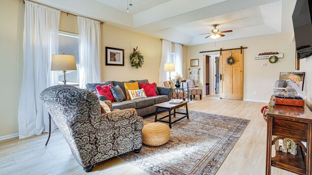 A spacious living room with a patterned sofa, a coffee table, and a rug. There are ceiling fans, a fireplace, and a door leading to another room. - Zanesville Apartment w/ Porch - 3 Mi to Downtown! (Zanesville)