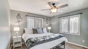 A bedroom with a bed, two bedside tables, a ceiling fan, and two windows with blinds.