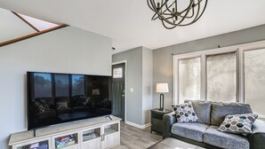 A living room with a flat-screen TV, a sofa, a coffee table, and a cabinet with board games.