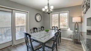 A dining area with a large table, chairs, a chandelier, and a clock on the wall.