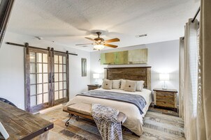 Un dormitorio con una cama grande, un ventilador de techo, un banco de madera, un escritorio y un cristalero corredera.
