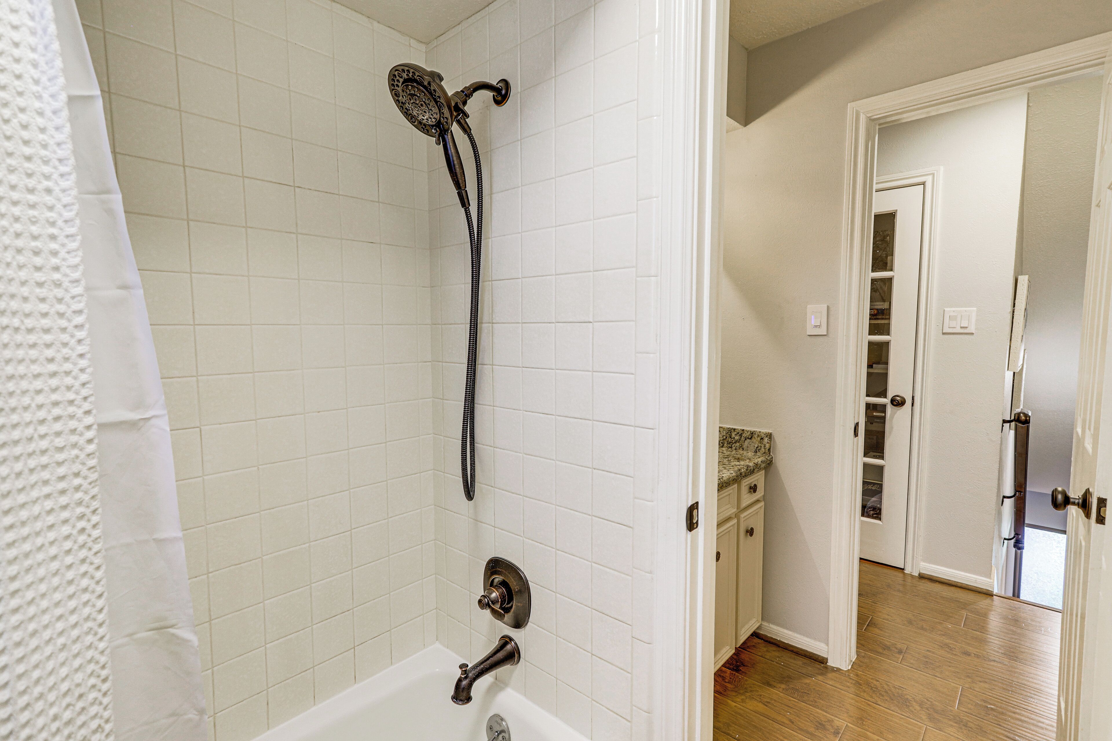A bathroom with white tiled walls, a bathtub, and a showerhead.
