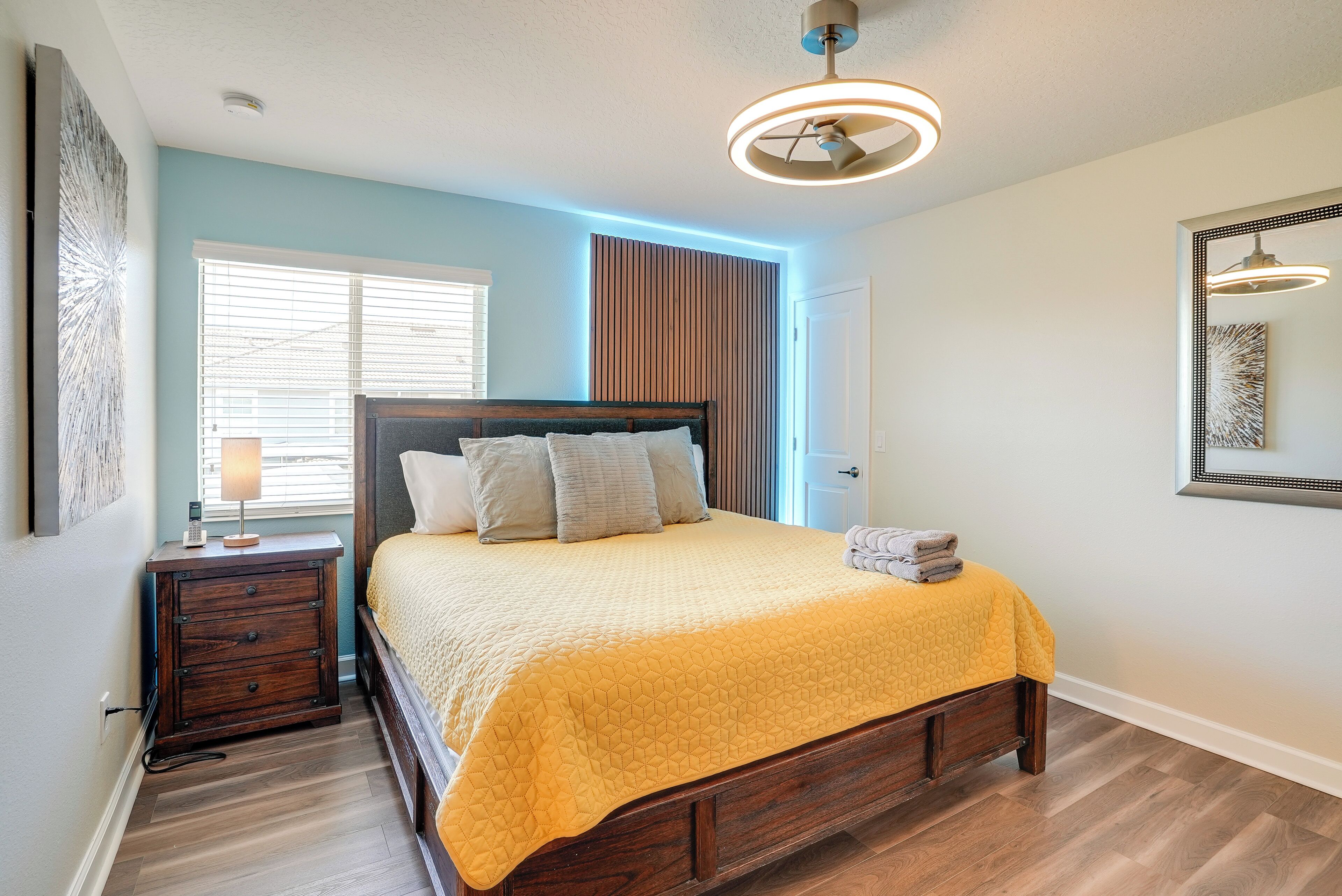 A bedroom with a wooden bed, a nightstand, a lamp, and a ceiling fan.