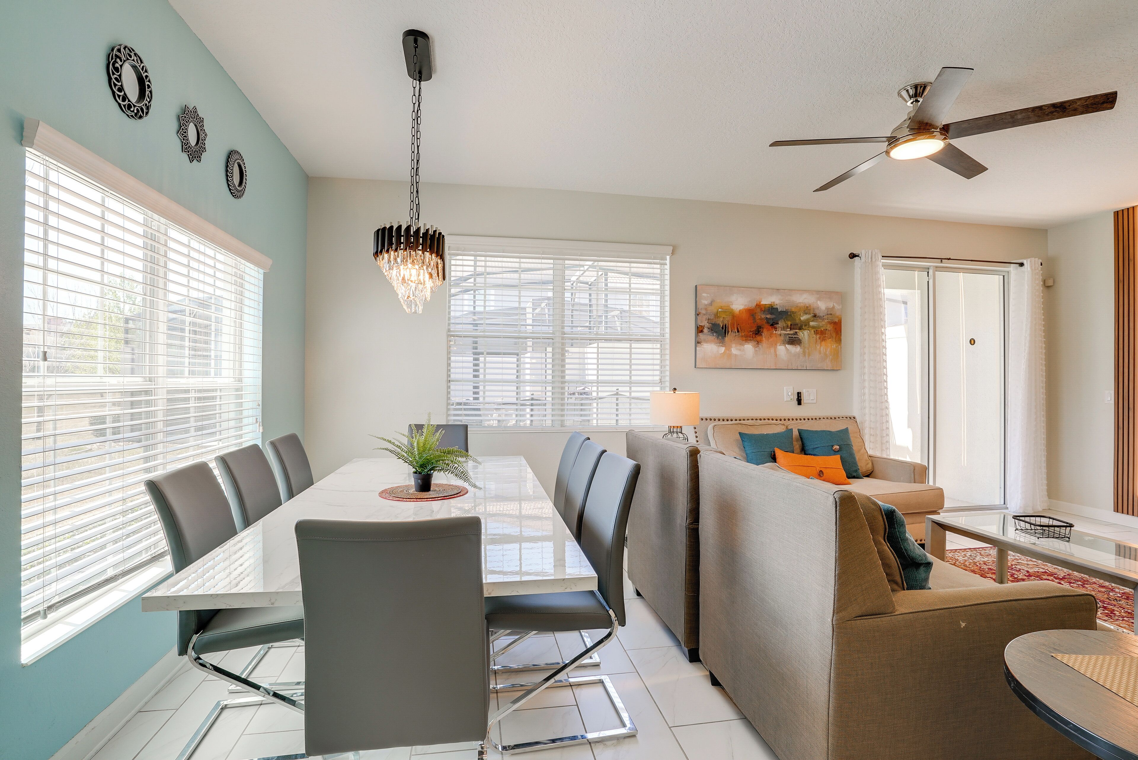A modern living room with a dining area, a ceiling fan, and a large window with blinds.