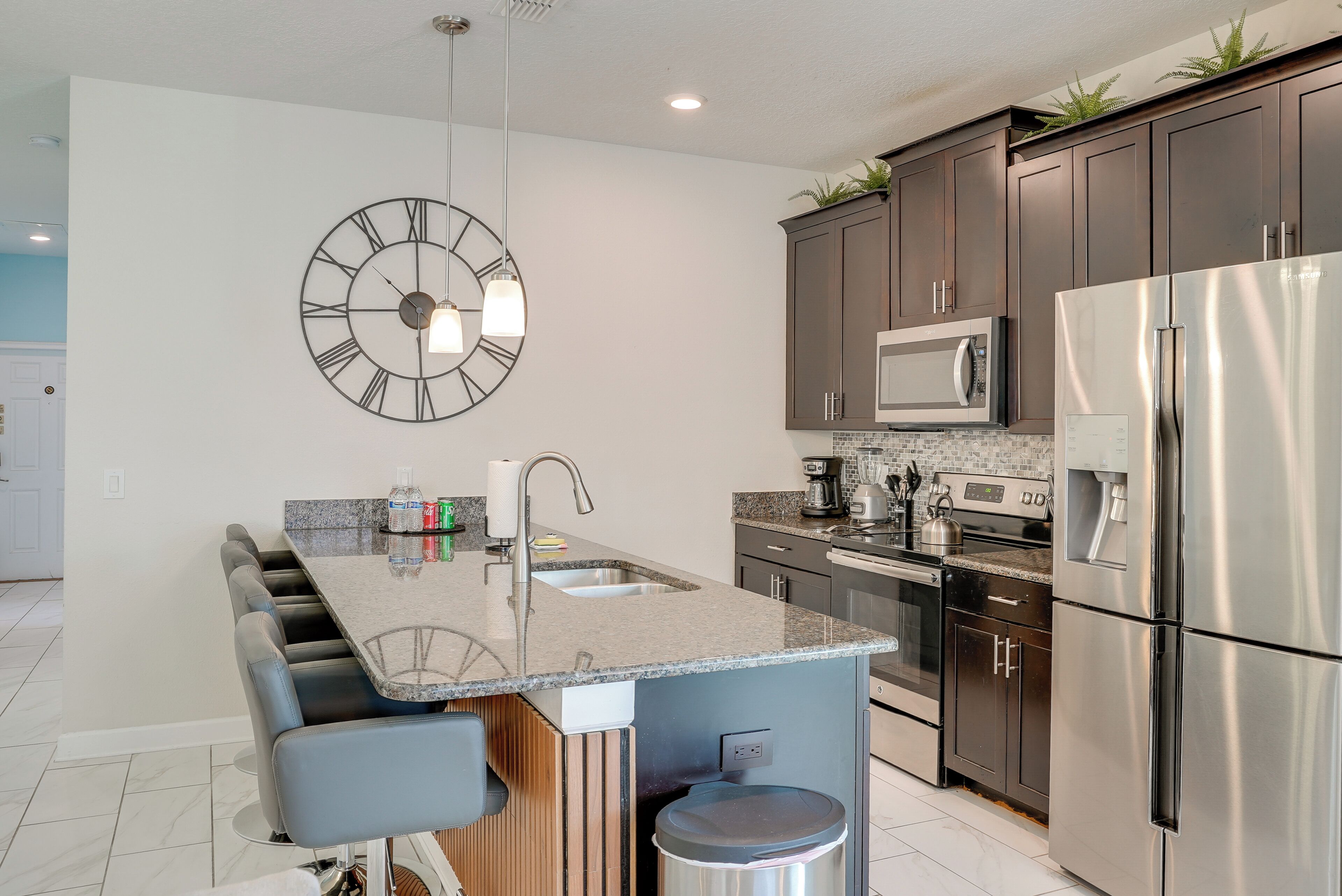 A modern kitchen with a central island, stainless steel appliances, and a large wall clock.