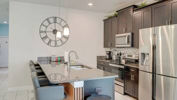 A modern kitchen with a central island, stainless steel appliances, and a large wall clock.
