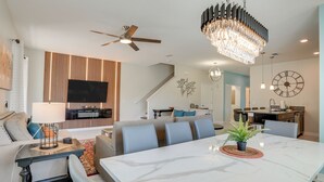 Een moderne woonkamer met een grote televisie, een eettafel en een kroonluchter.