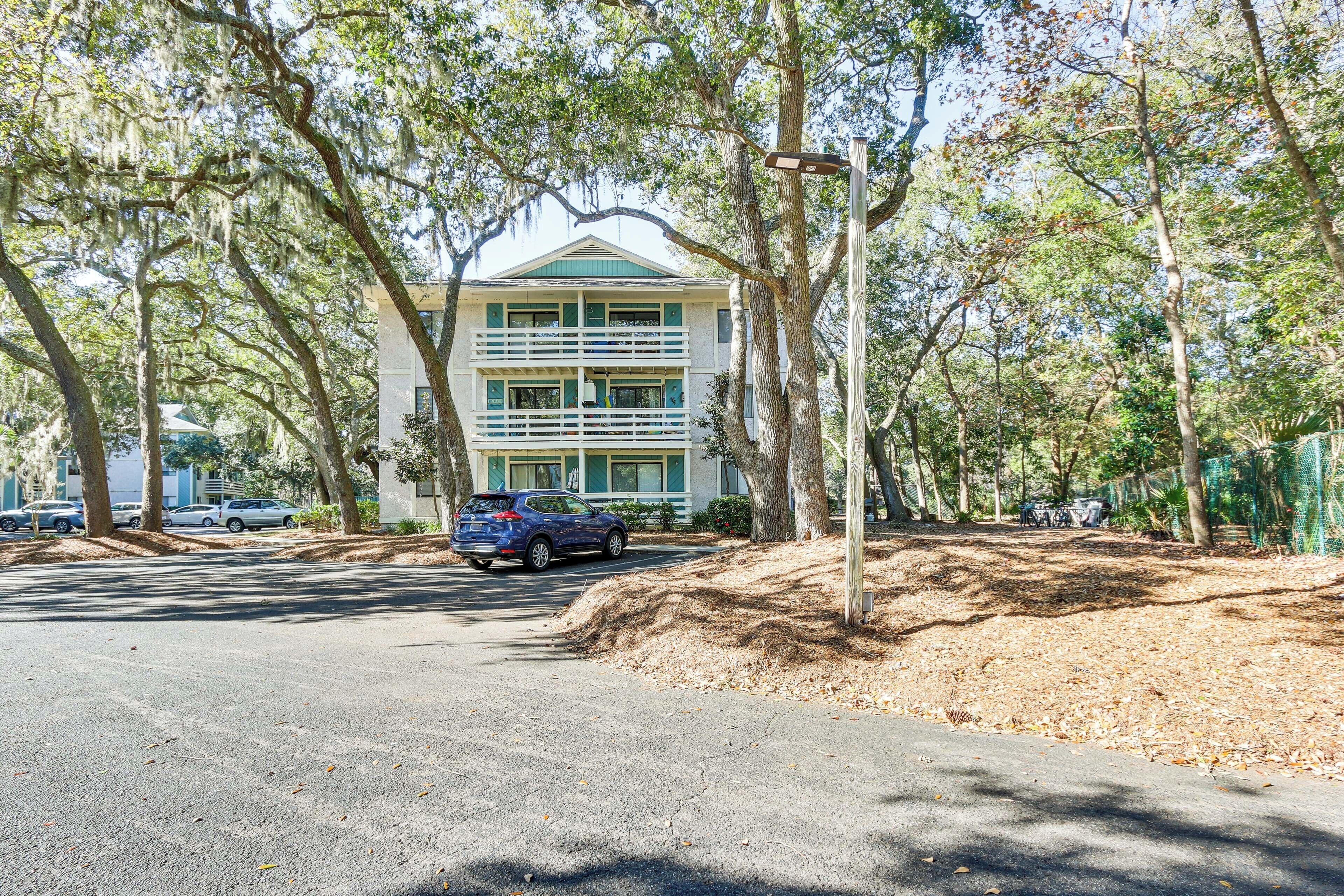 A two-story building with a balcony, surrounded by trees and parked cars.