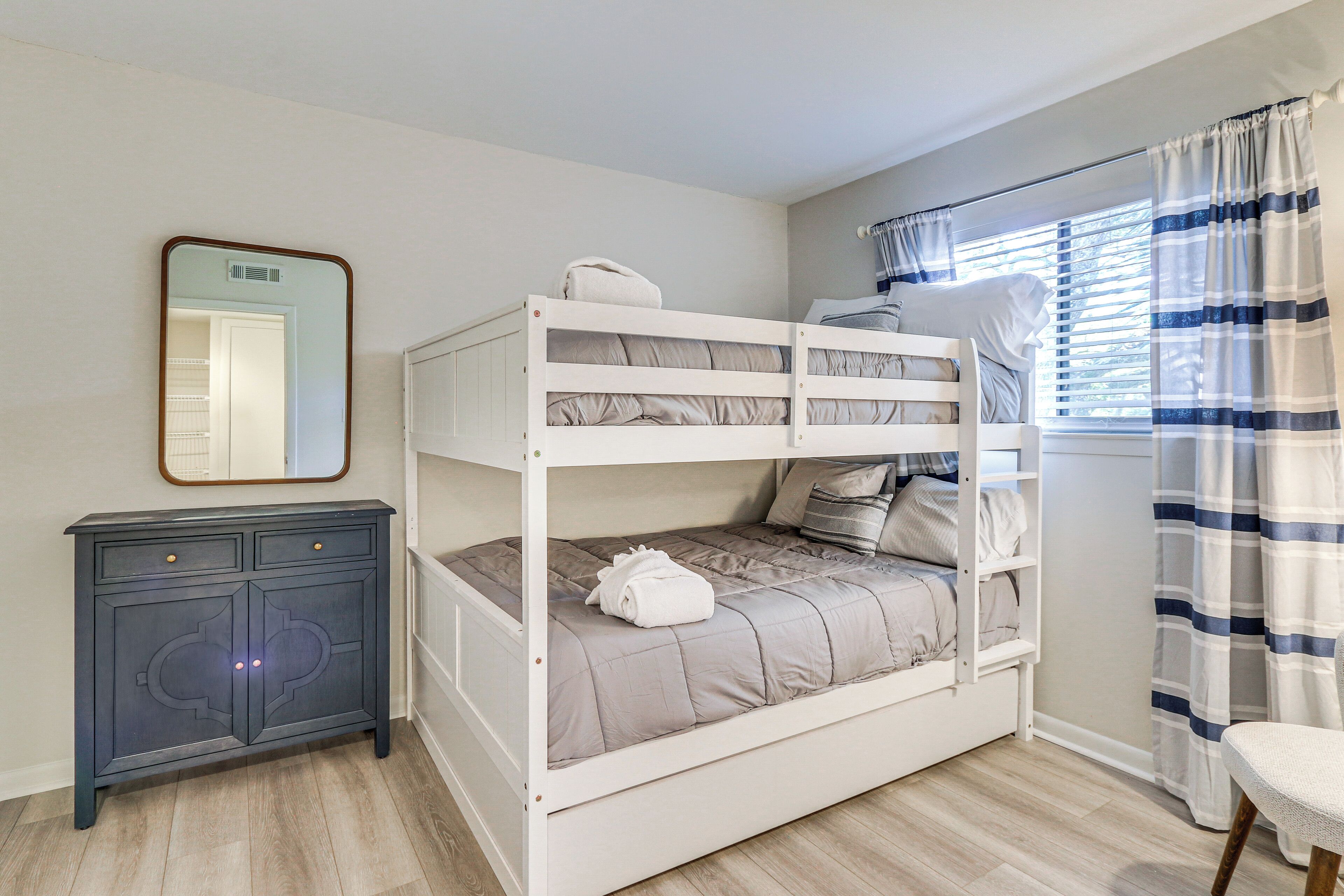 A bunk bed with a mirror above it, a dark cabinet, and a window with curtains.