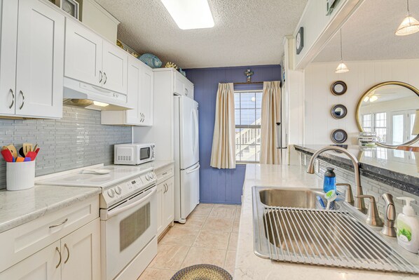 A modern kitchen with white cabinets, a microwave, a stove, and a sink. - Gulf Coast Views: Waterfront Surfside Beach Home! (Freeport)