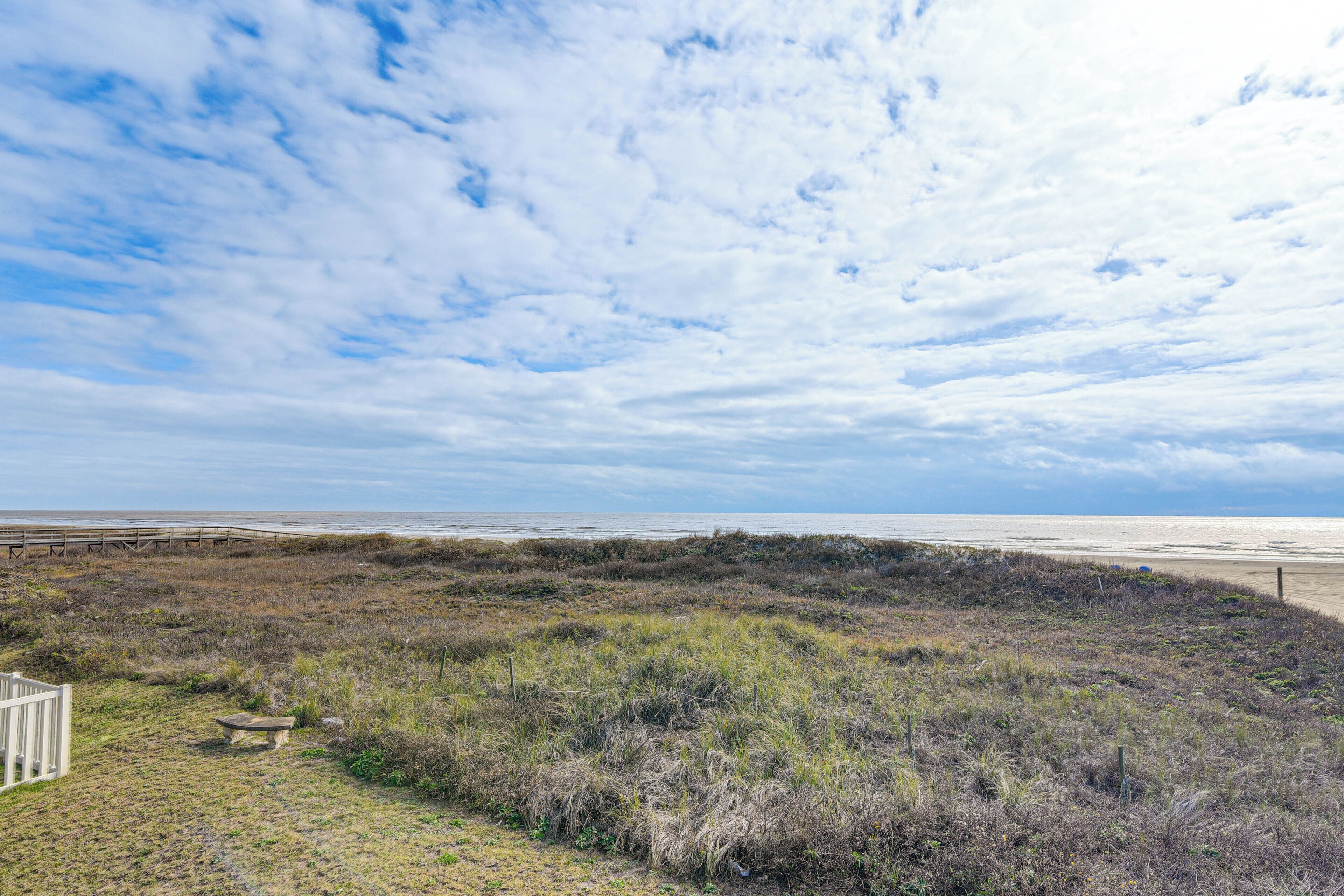A coastal landscape with a wooden fence, a bench, and a view of the beach and ocean.