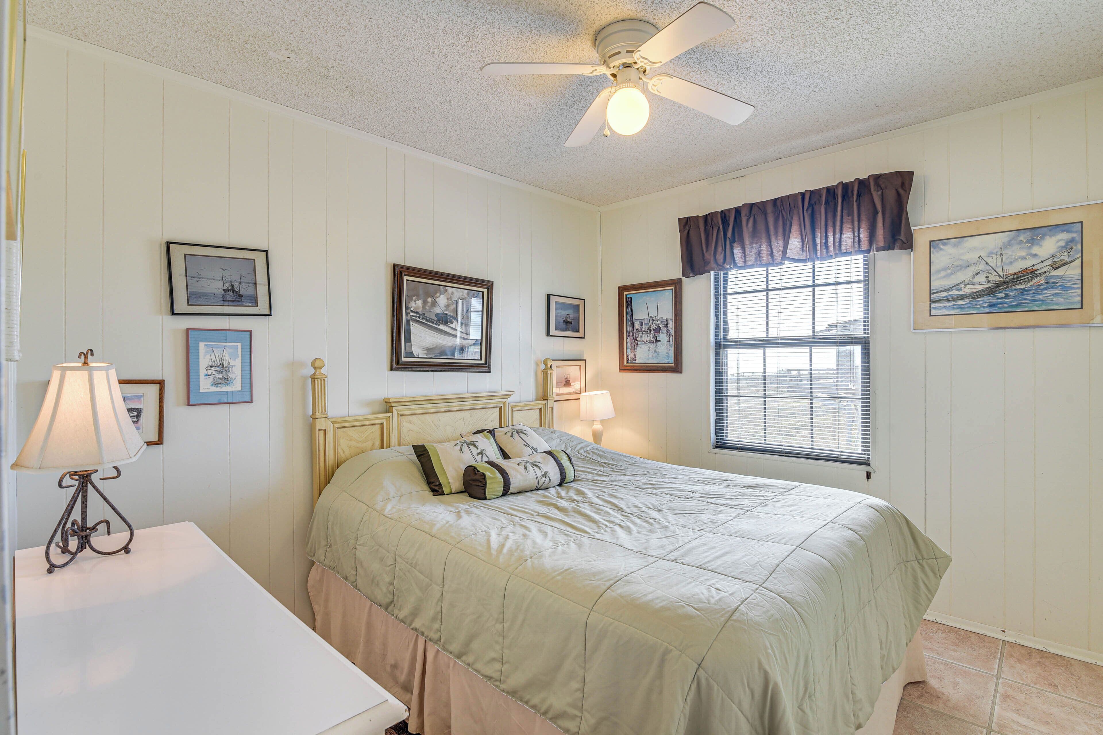 Une chambre à coucher comprenant un lit, une table de chevet, une lampe, un ventilateur de plafond et des tableaux encadrés accrochés aux murs.