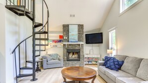 A living room with a fireplace, a round wooden coffee table, a sofa, and a spiral staircase. - 'gabbi's Getaway' - Little Tallapoosa River Cabin (Wedowee)