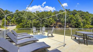 A rooftop terrace with lounge chairs, a table, and chairs overlooking a lake and forested hills.