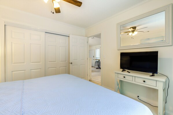 A bedroom with a large bed, a TV on a white dresser, and a ceiling fan.