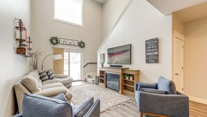 Een ruime woonkamer met een open haard, een grote flatscreen televisie en een gezellige zithoek met twee fauteuils en een bank.