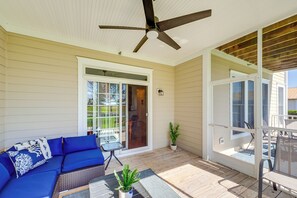 A covered patio with a ceiling fan, a blue sofa, a table with chairs, and a sliding glass door leading to a deck.