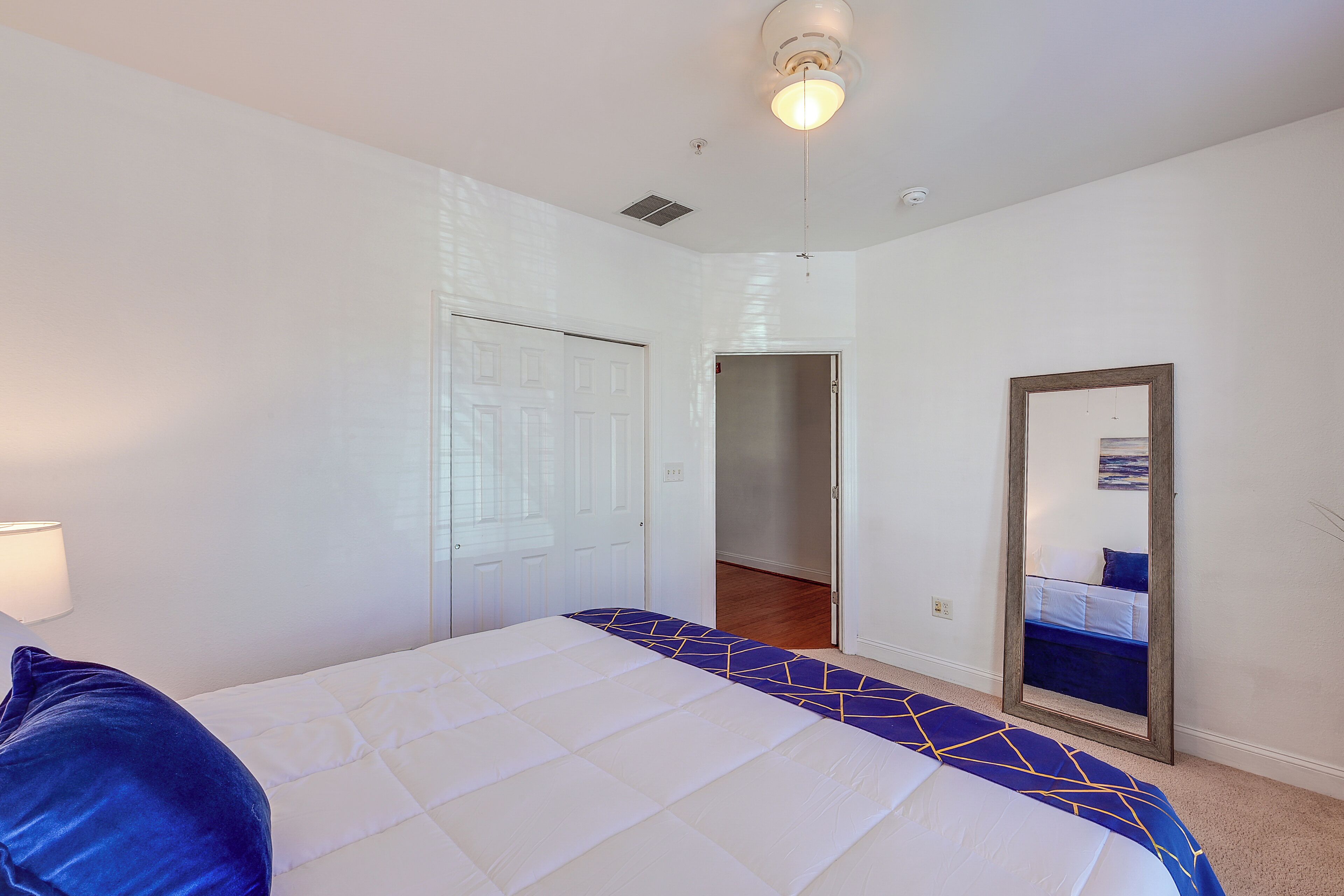 A bedroom with a bed, a door, a mirror, and a ceiling light.