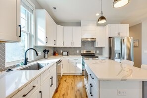A modern kitchen with white cabinetry, a large island, stainless steel appliances, and a herringbone-patterned backsplash. - Family Home on Oak Island: 1 Mi to Beach & Pier! (Oak Island)