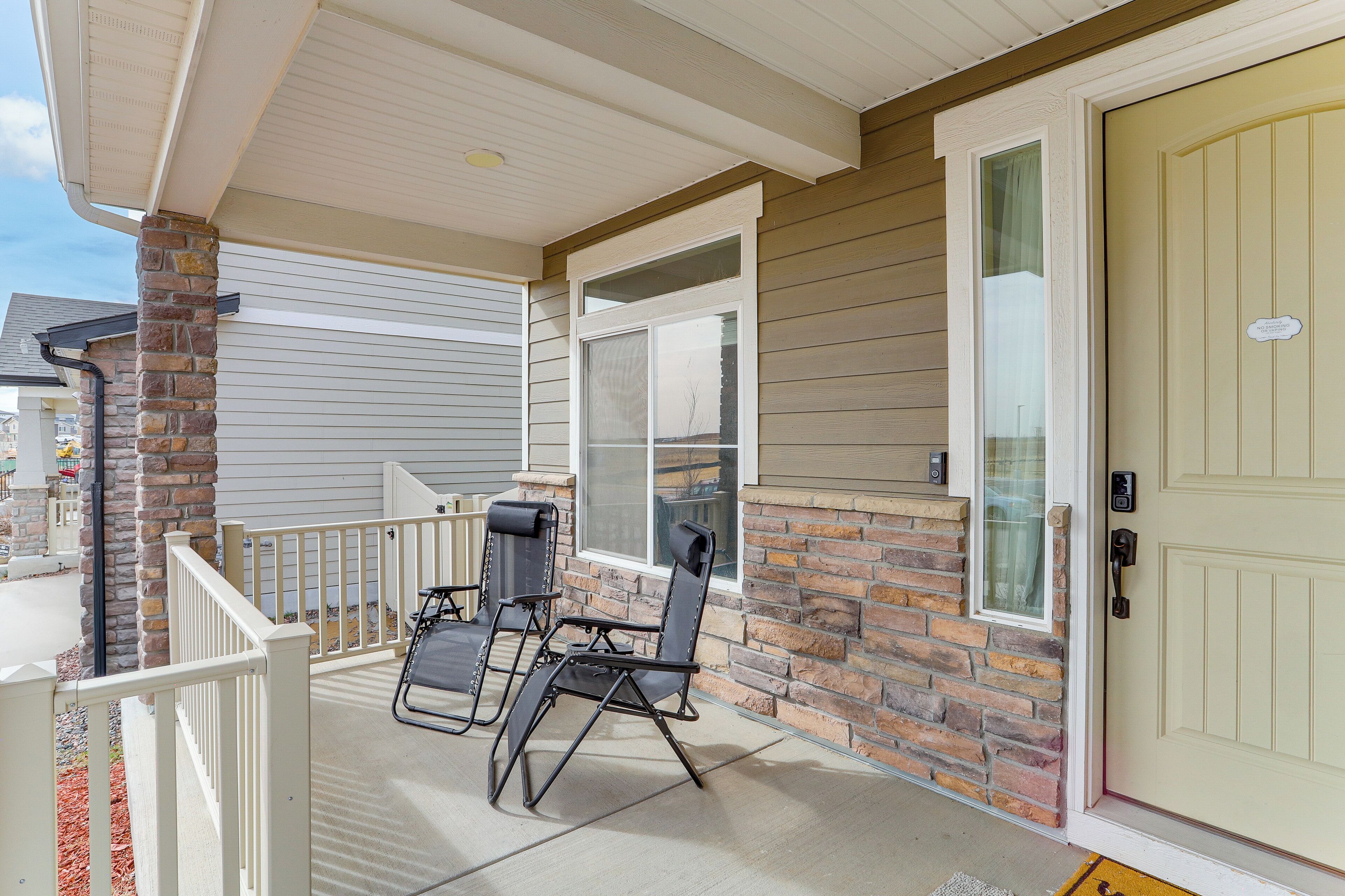 A covered porch with two folding chairs and a small table, a door with a mailbox, and a brick wall.