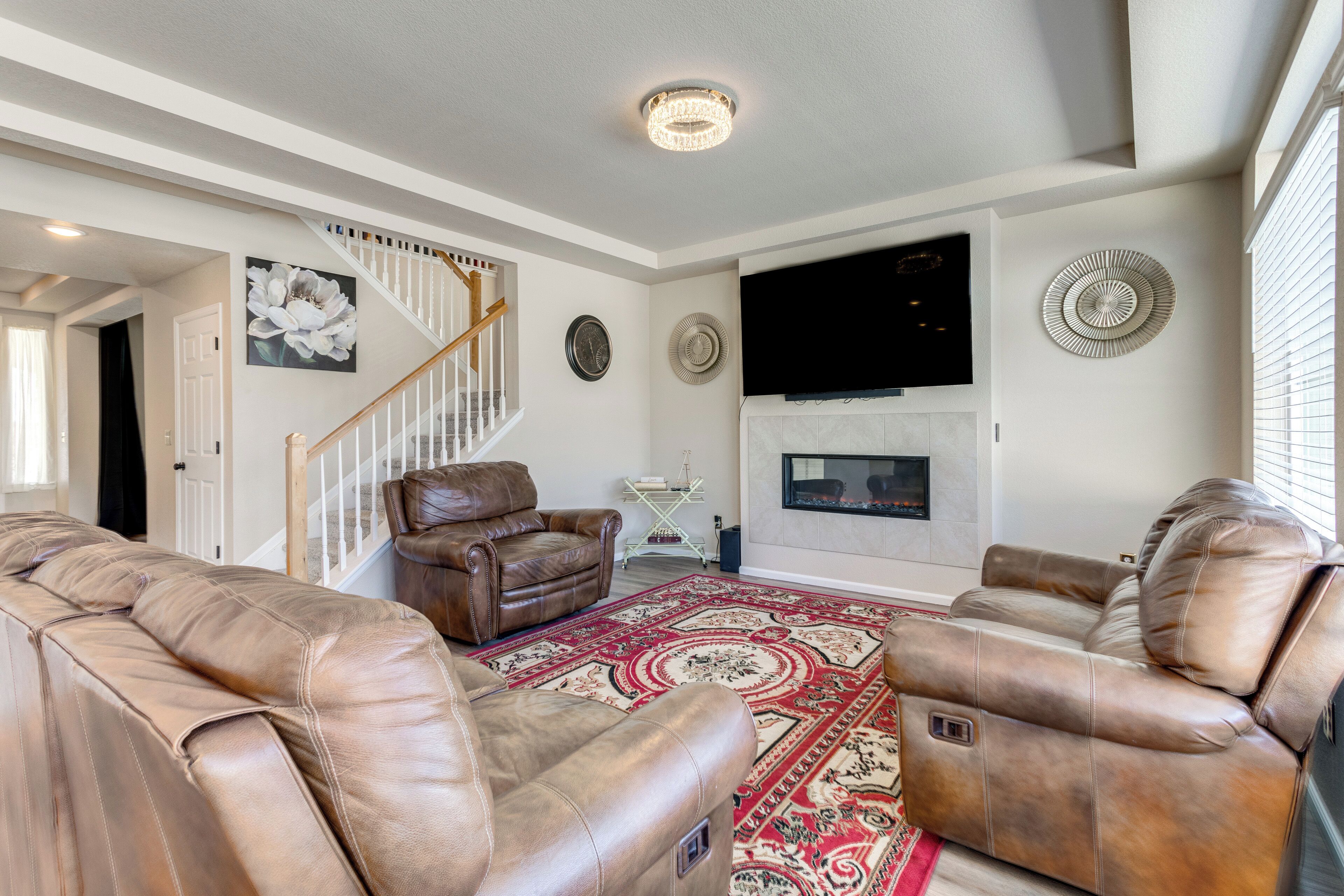 A living room with leather recliners, a large rug, a fireplace, and a staircase.