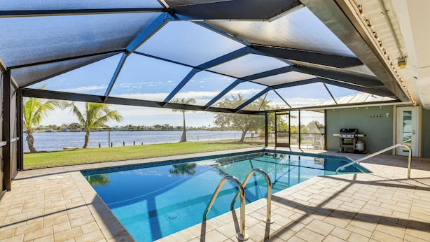Une piscine intérieure avec vue sur l’eau et les palmiers, entourée d’une terrasse couverte.