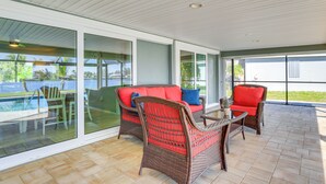Un patio couvert, aménagé avec des meubles en osier et doté d’une porte vitrée donnant accès à une piscine.