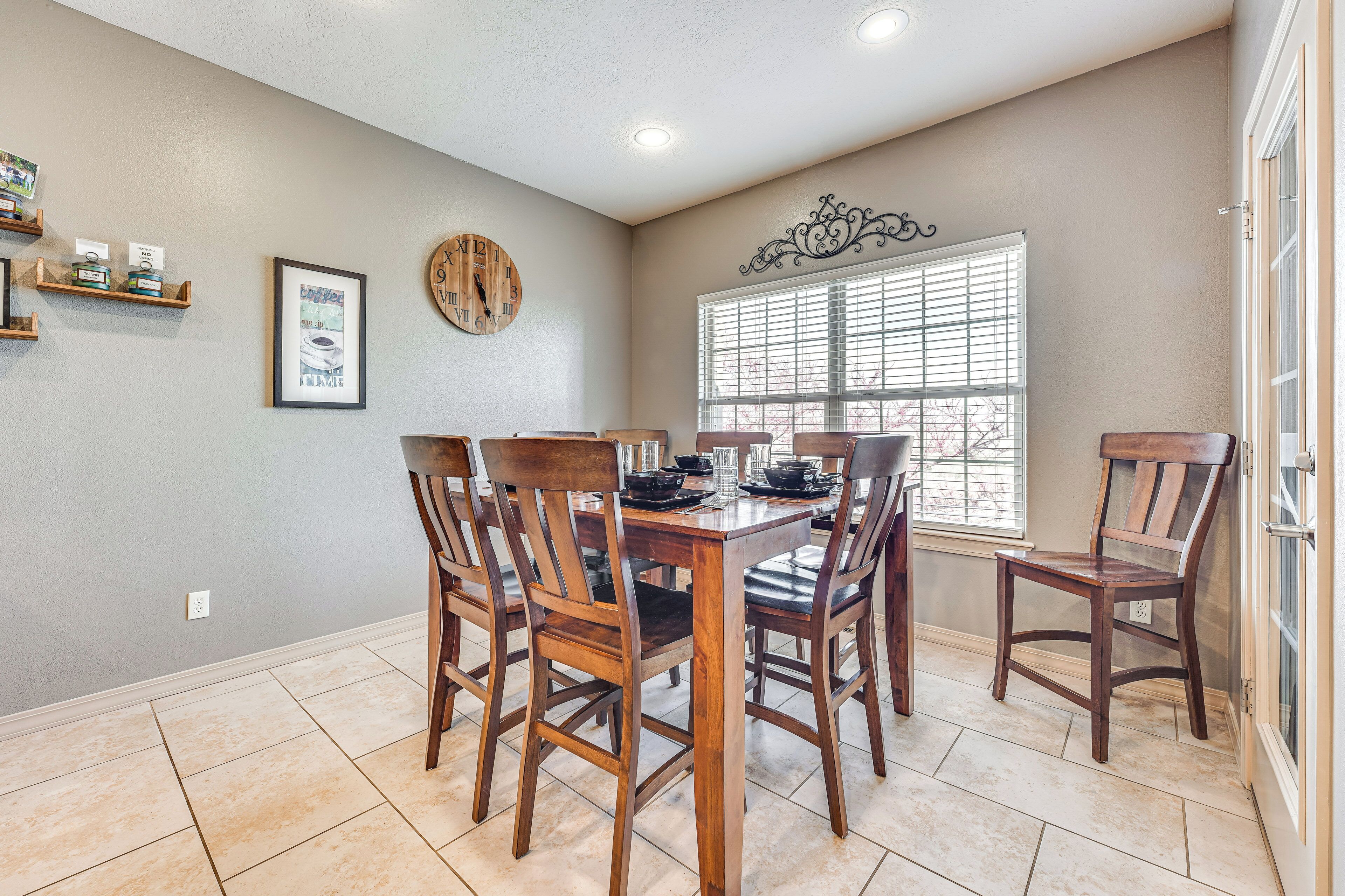 A dining area with a wooden table and chairs, a clock on the wall, and a window with blinds.