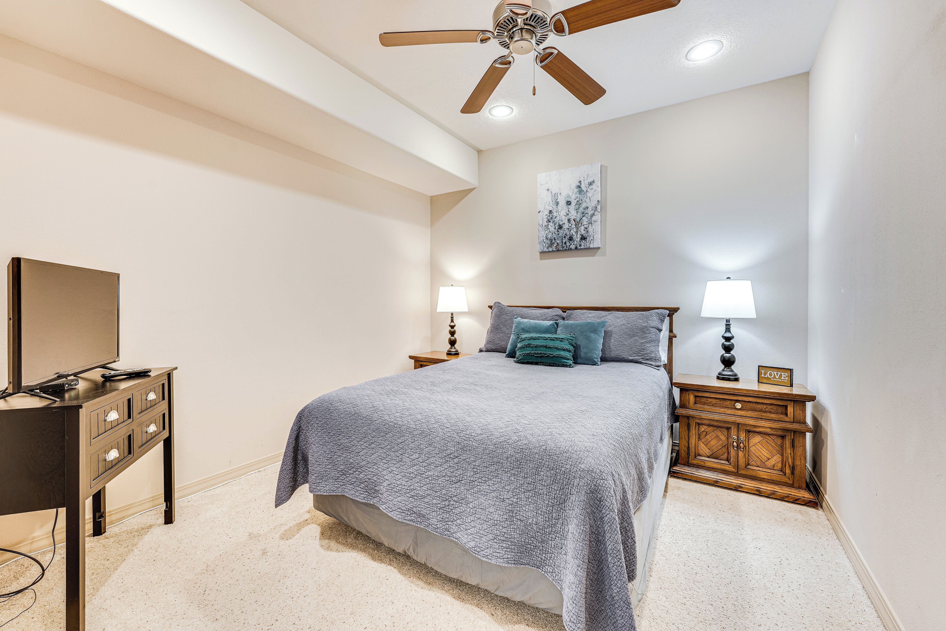 A bedroom with a bed, nightstands, a desk, and a ceiling fan.