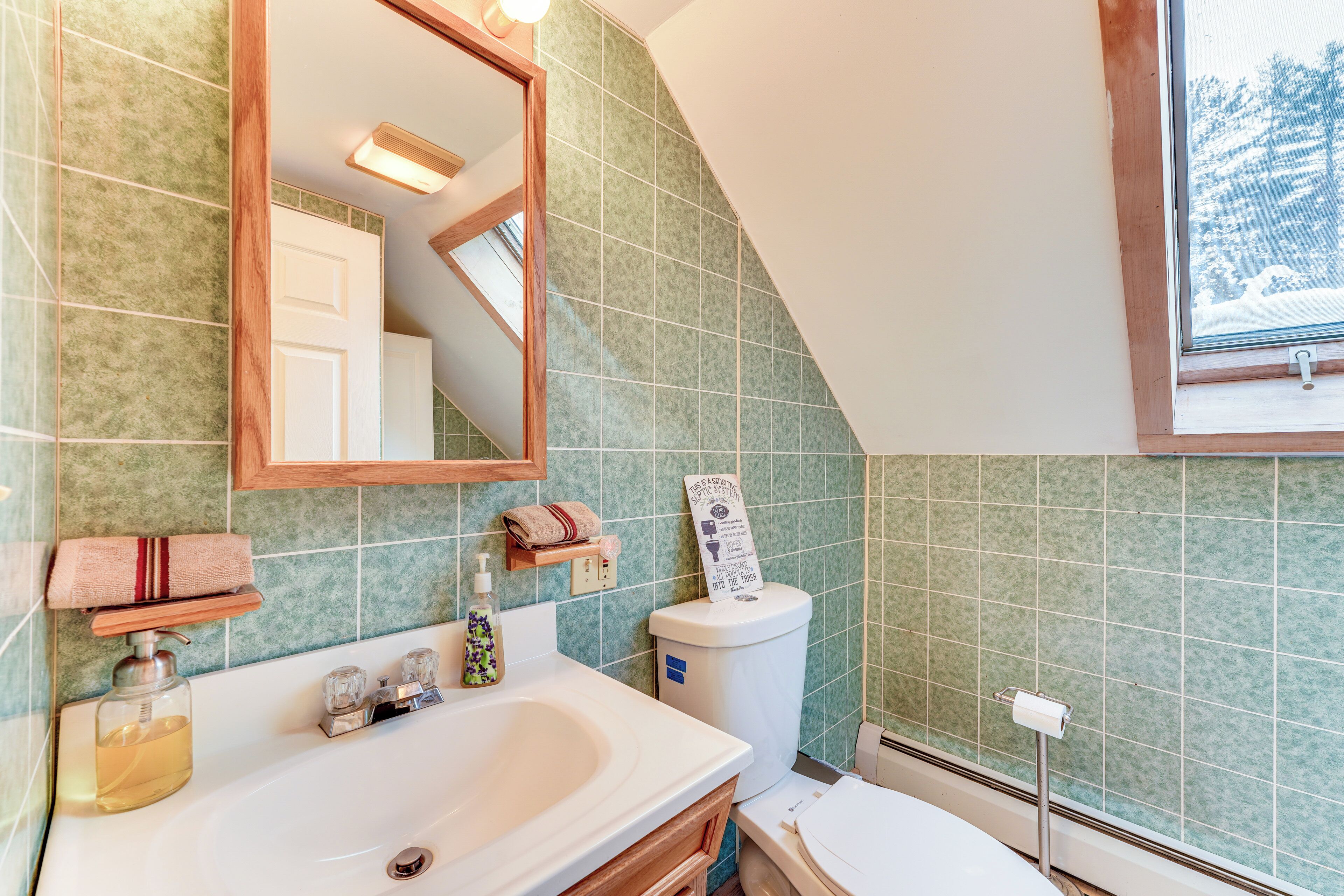 A bathroom with a large mirror, a sink, and a toilet. There is a towel rack with a towel and a soap dispenser on the sink.