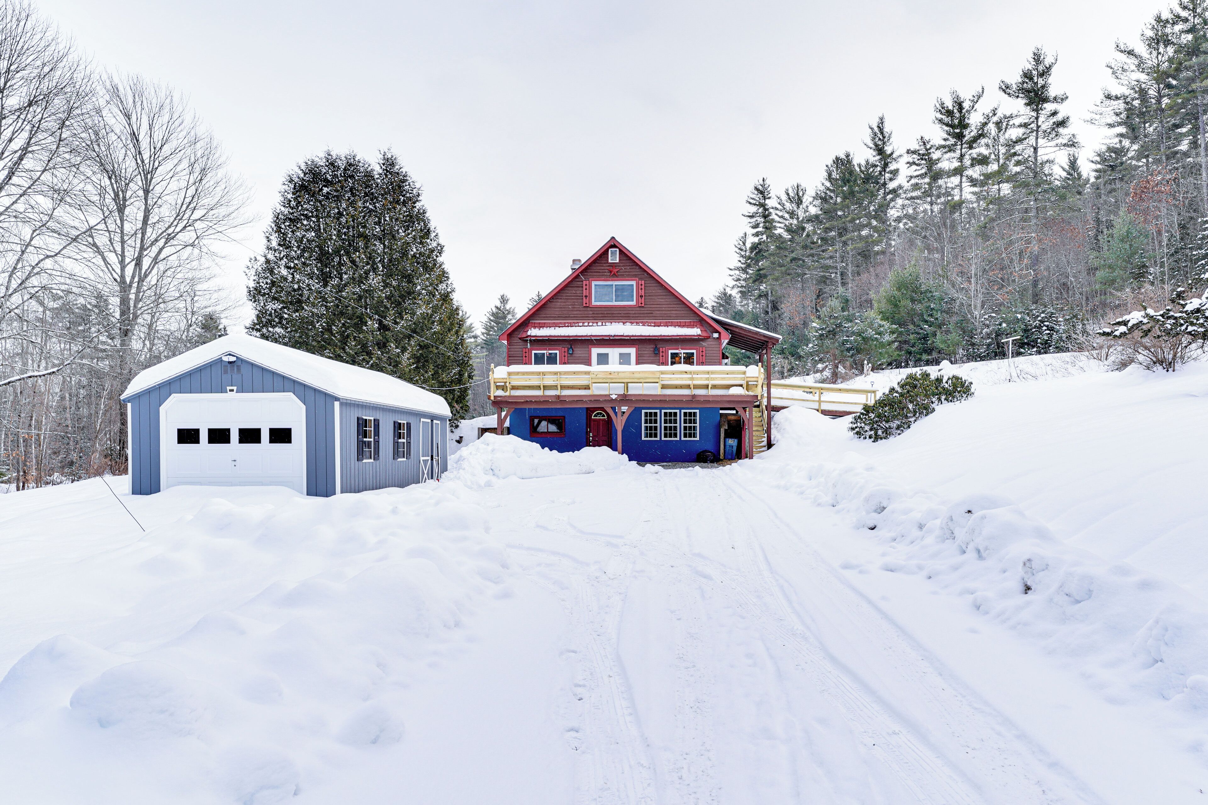 Ein zweistöckiges Haus mit rotem Dach und blauen Wänden, umgeben von schneebedecktem Boden und Bäumen.