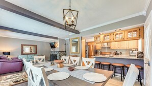 A modern kitchen with wooden cabinets, a dining area with a large table, and a living room with a purple sofa.