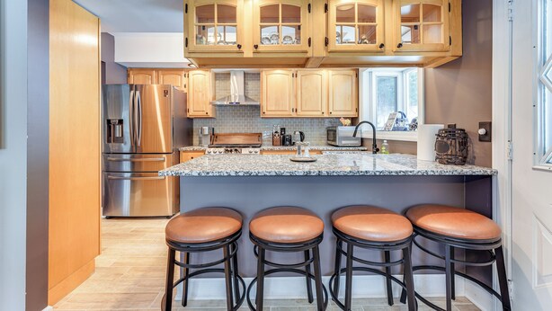 A modern kitchen with wooden cabinets, stainless steel appliances, a granite countertop, and bar stools.