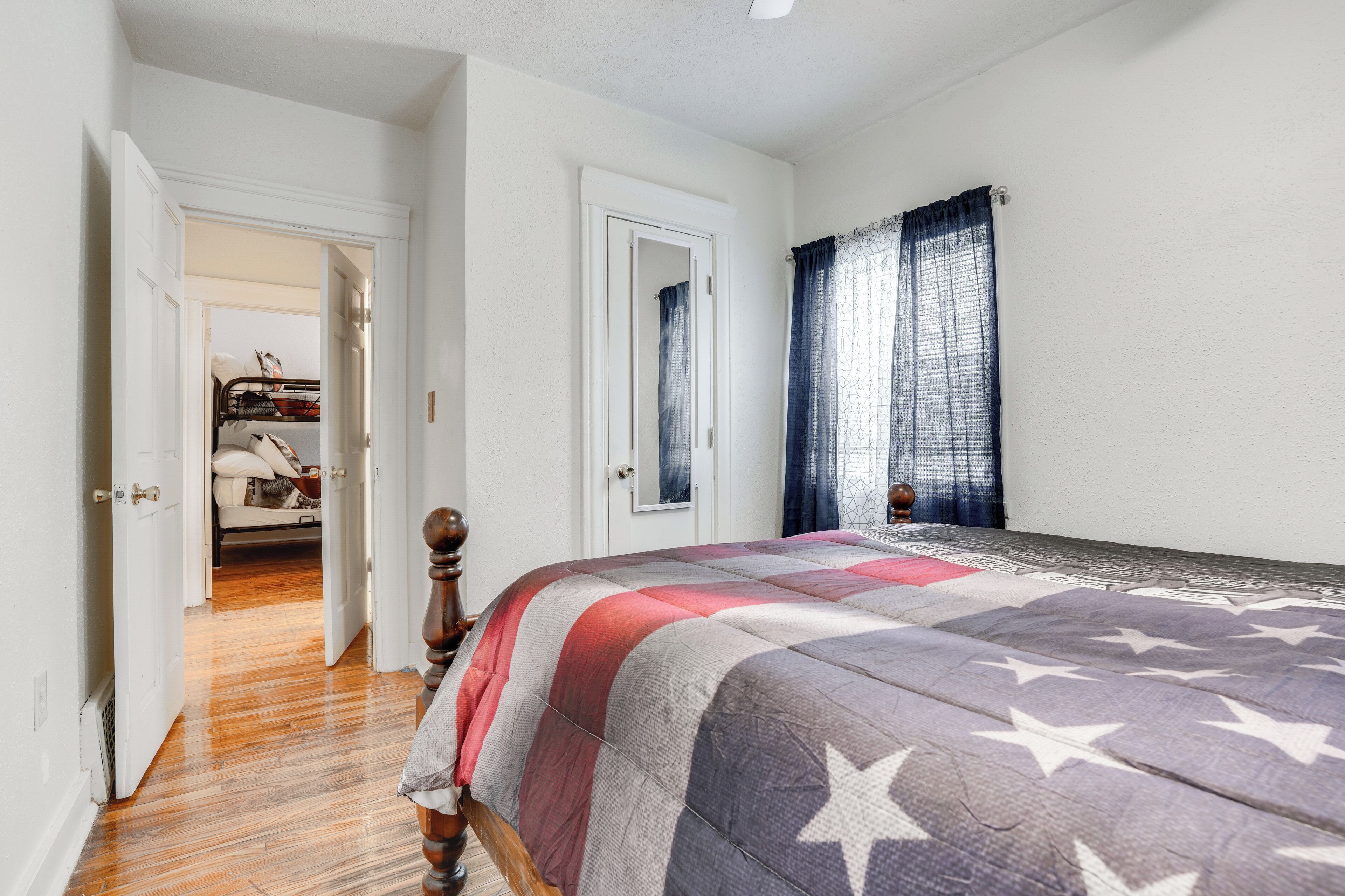 A bedroom with a bed, wooden floor, white walls, and a door leading to another room.