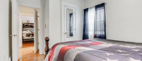 A bedroom with a bed, wooden floor, white walls, and a door leading to another room.