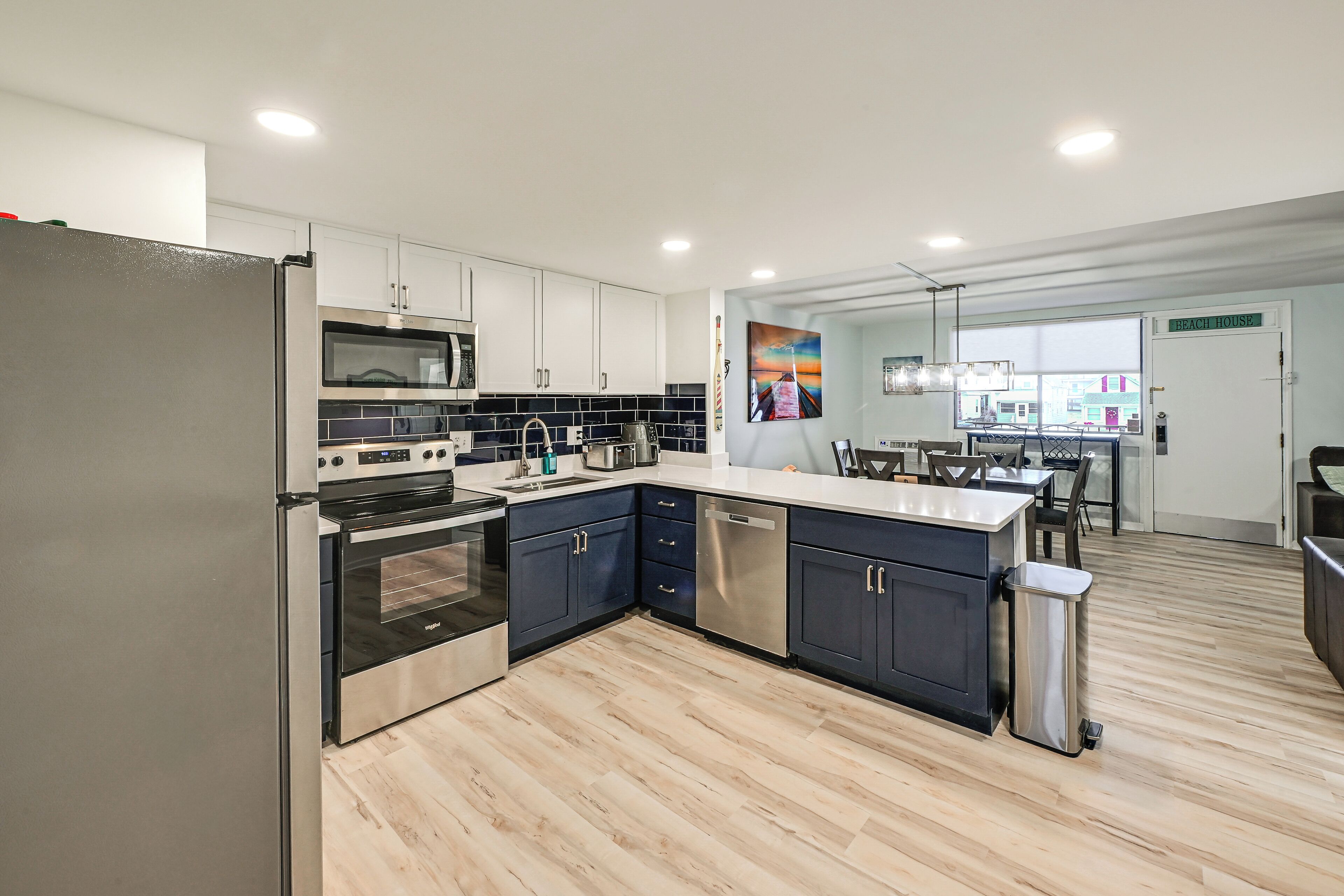A modern kitchen with stainless steel appliances, dark blue cabinets, and a wooden floor.