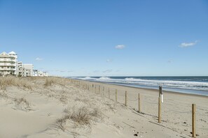 Una playa con una valla de madera, un edificio con varios balcones y el océano al fondo.