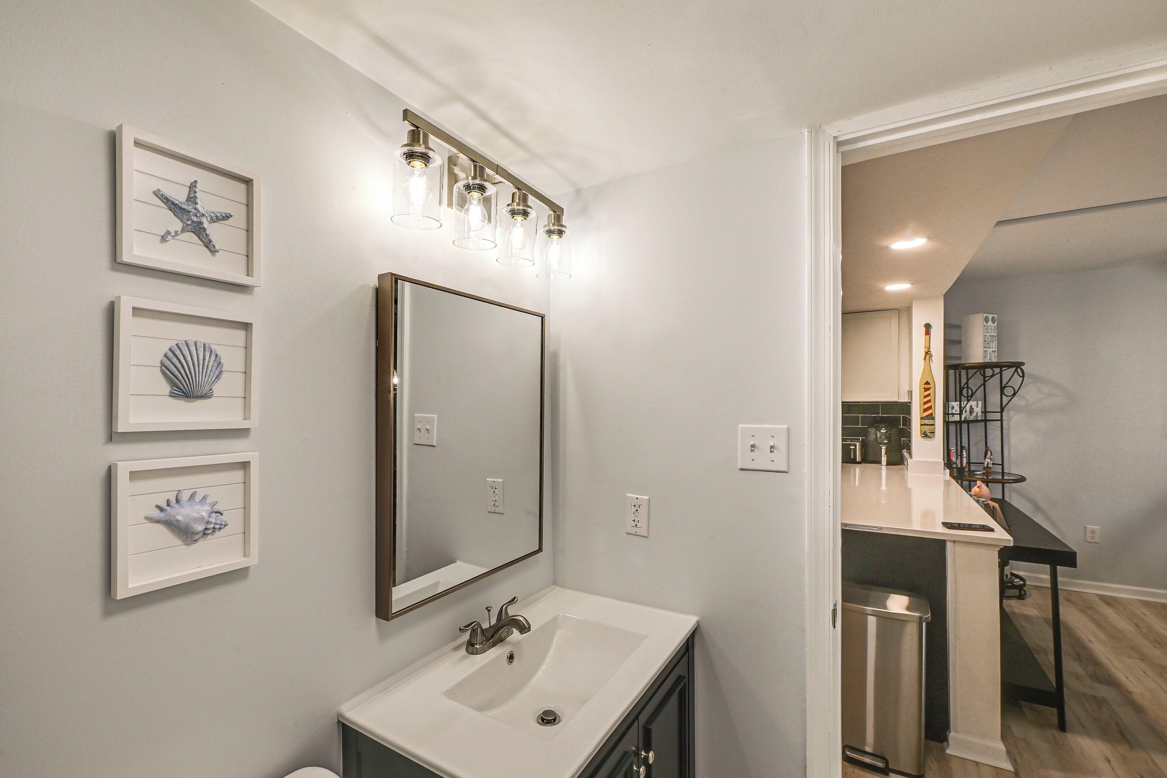A bathroom with a white sink, a large mirror, and framed artwork on the wall.