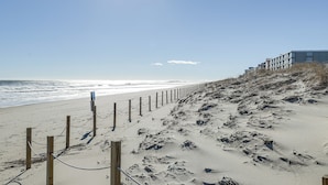 Una playa arenosa con una valla de madera y un edificio al fondo.