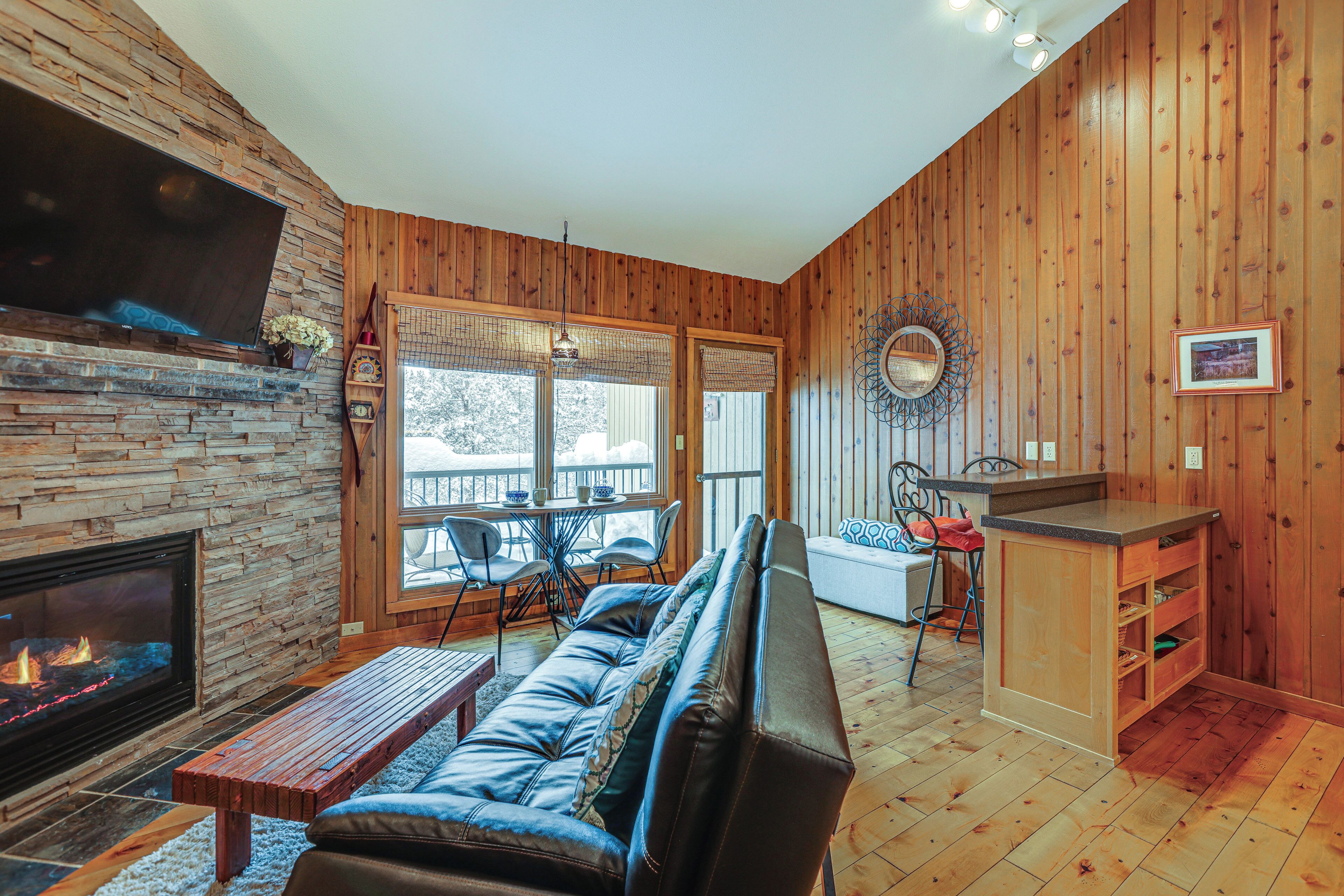A cozy living room with a stone fireplace, a leather sofa, and a wooden dining area.