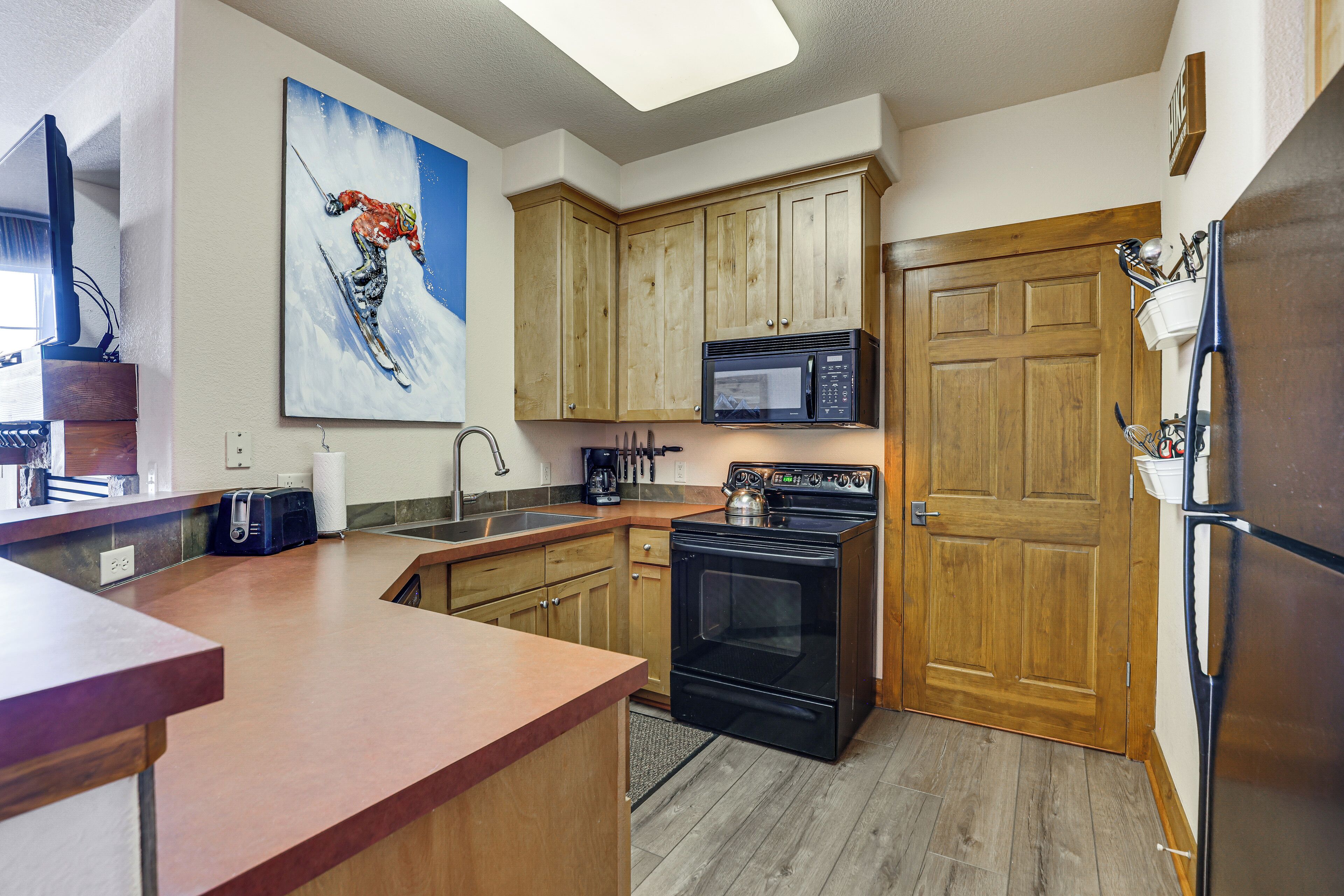 A kitchen with wooden cabinets, a black stove, a microwave, and a refrigerator.