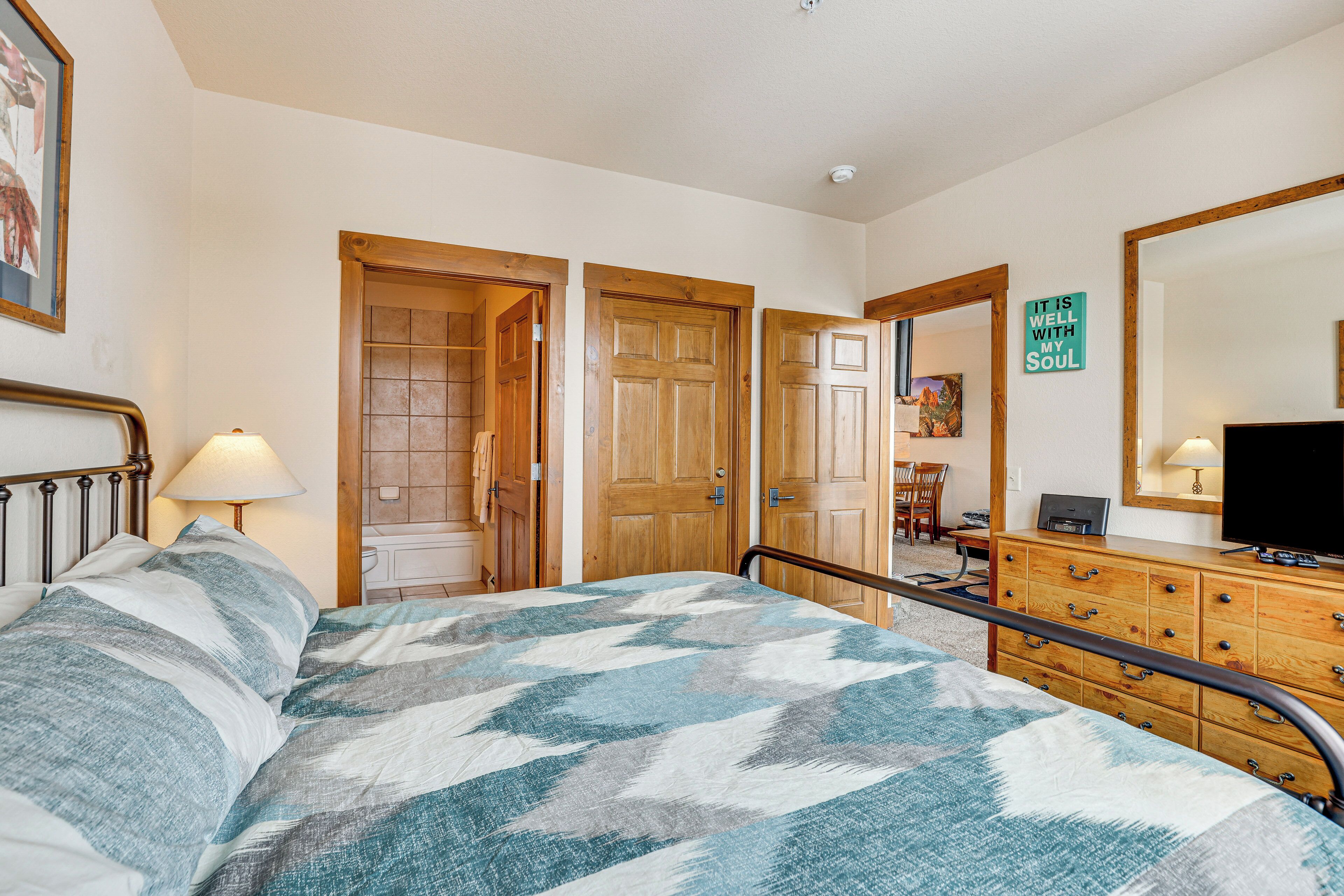 Une chambre à coucher avec un lit, des portes en bois, une commode, un miroir et un téléviseur.