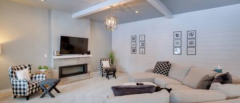 A modern living room with a sectional sofa, a fireplace, a TV, and a ceiling with recessed lighting.