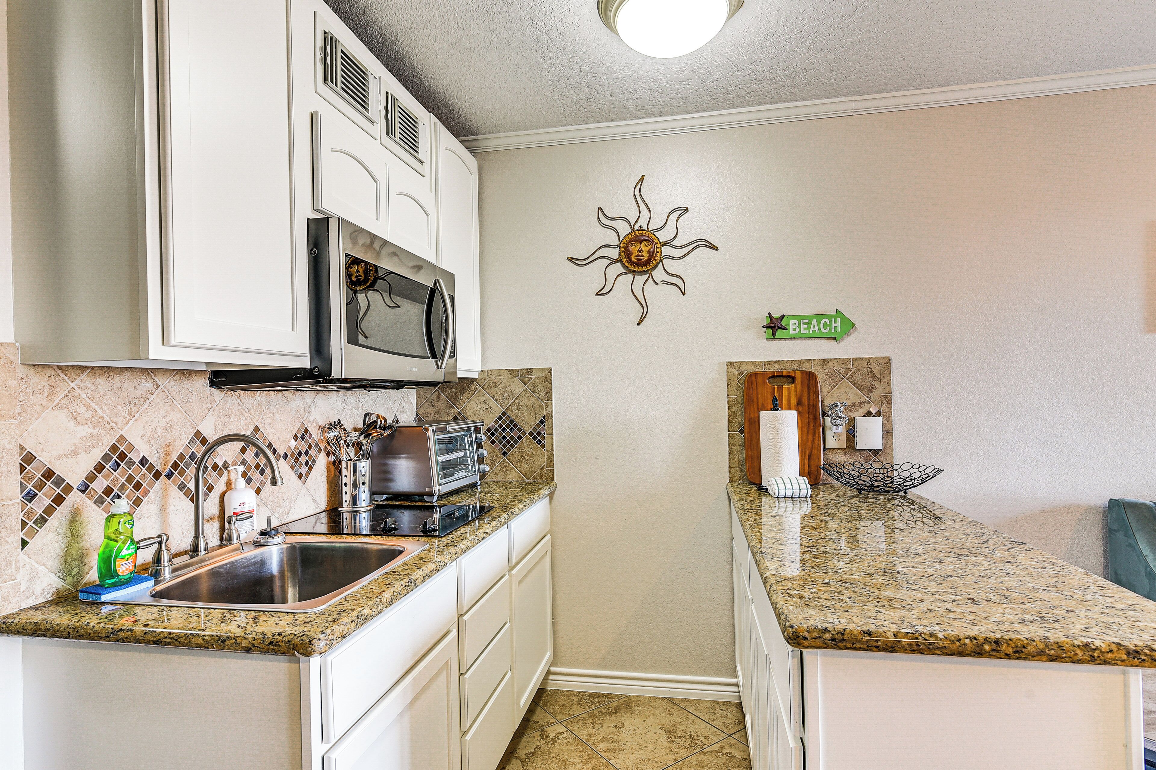 A kitchen with white cabinets, a granite countertop, a microwave, a toaster, and a sink.