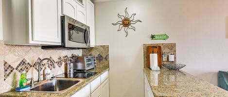 A kitchen with white cabinets, a granite countertop, a microwave, a toaster, and a sink.